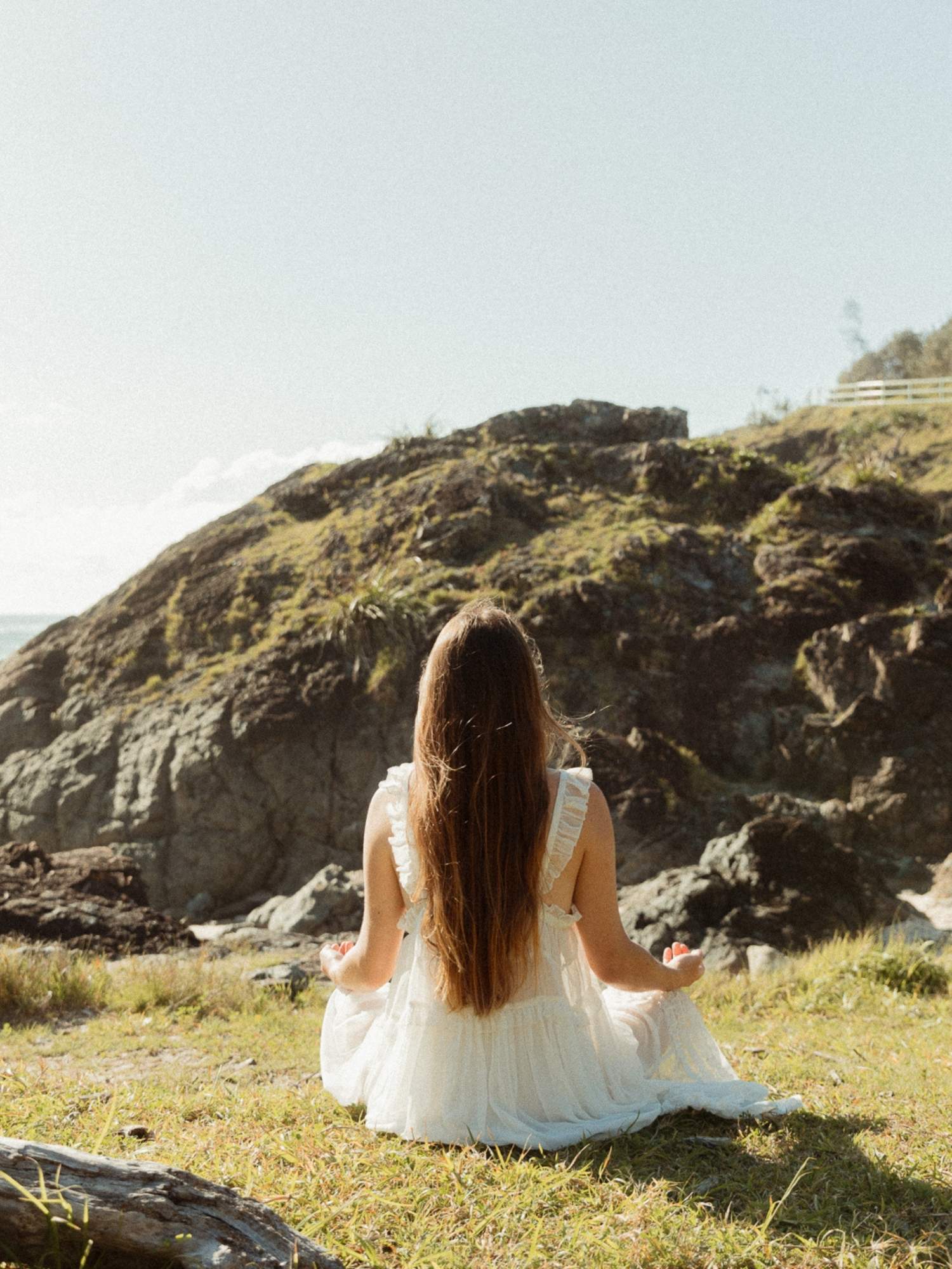 Em seated in meditation on the grass, facing a rocky headland